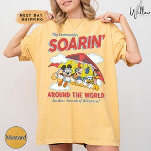 A woman wearing a yellow t-shirt with a graphic of Mickey Mouse and Goofy on a parachute, along with the text "SOARIN' AROUND THE WORLD" and "Fearless Pursuit of Adventure!".