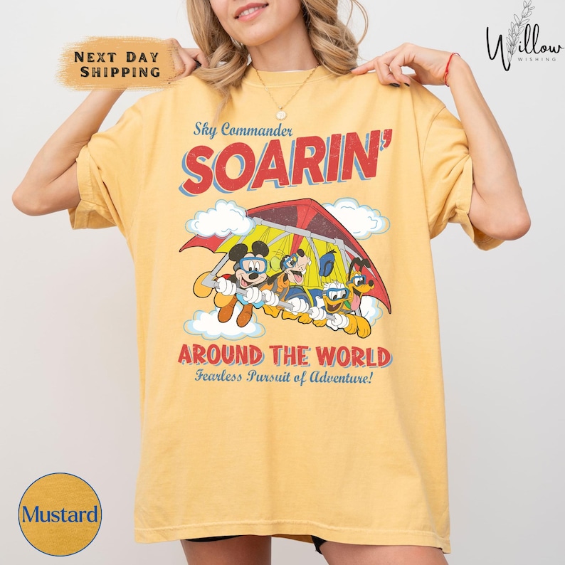 A woman wearing a yellow t-shirt with a graphic of Mickey Mouse and Goofy on a parachute, along with the text "SOARIN' AROUND THE WORLD" and "Fearless Pursuit of Adventure!".