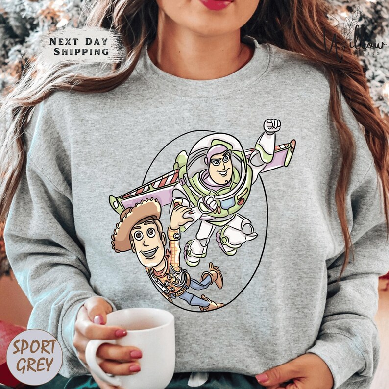 A woman wearing a gray sweatshirt with a cartoon image of Buzz Lightyear and Woody from Toy Story printed on it.