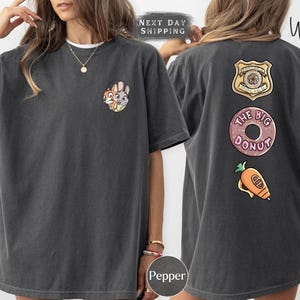 A woman wearing a gray t-shirt with various cartoon characters and designs, including a police badge, a donut, and a carrot.