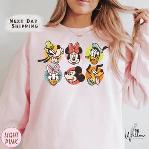 A woman wearing a pink sweatshirt with a graphic of Disney characters on it.