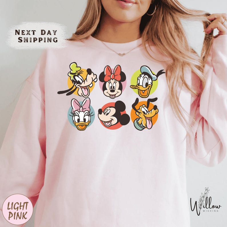 A woman wearing a pink sweatshirt with a graphic of Disney characters on it.