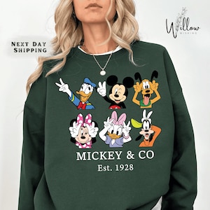 A woman wearing a green sweatshirt with a graphic of Disney characters Mickey Mouse and Co.