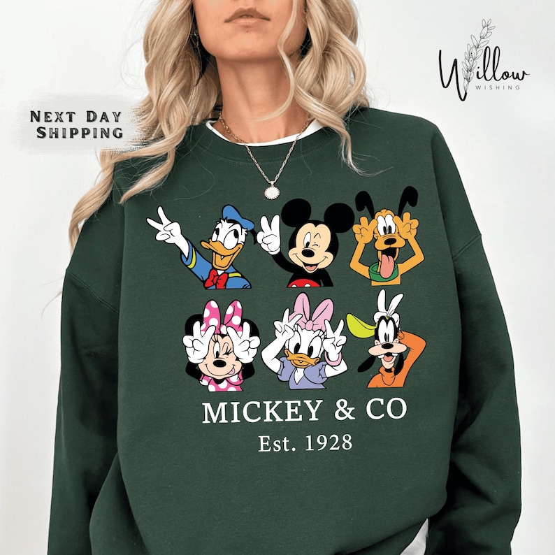A woman wearing a green sweatshirt with a graphic of Disney characters Mickey Mouse and Co.