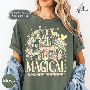 A woman wearing a green t-shirt with a colorful graphic design featuring various Disney-themed elements such as Mickey Mouse, Eiffel Tower, and other iconic landmarks.