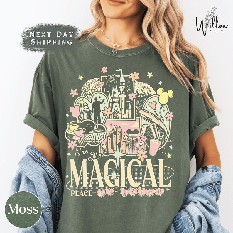 A woman wearing a green t-shirt with a colorful graphic design featuring various Disney-themed elements such as Mickey Mouse, Eiffel Tower, and other iconic landmarks.