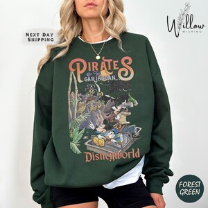 A woman wearing a green sweatshirt with a colorful graphic of Disney characters and the text "Pirates of the Caribbean: The Caribbean" printed on it.