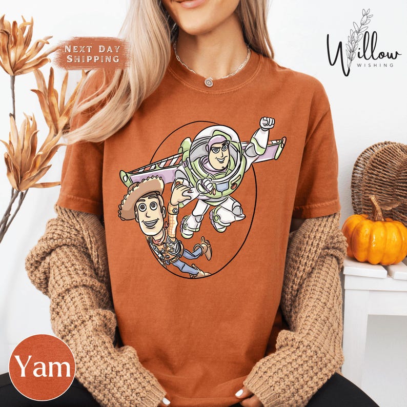 A woman wearing a t-shirt with a cartoon character from the Toy Story franchise, specifically Buzz Lightyear, is sitting in front of a pumpkin.