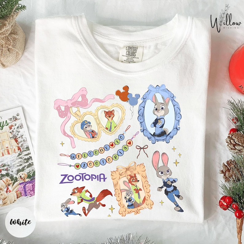 A white t-shirt with a colorful graphic design featuring various cartoon animal characters, including a rabbit, fox, and duck, along with decorative elements such as ribbons and bows.