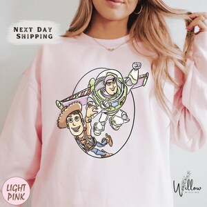 A woman wearing a pink sweatshirt with a cartoon illustration of Buzz Lightyear and Woody from Toy Story.