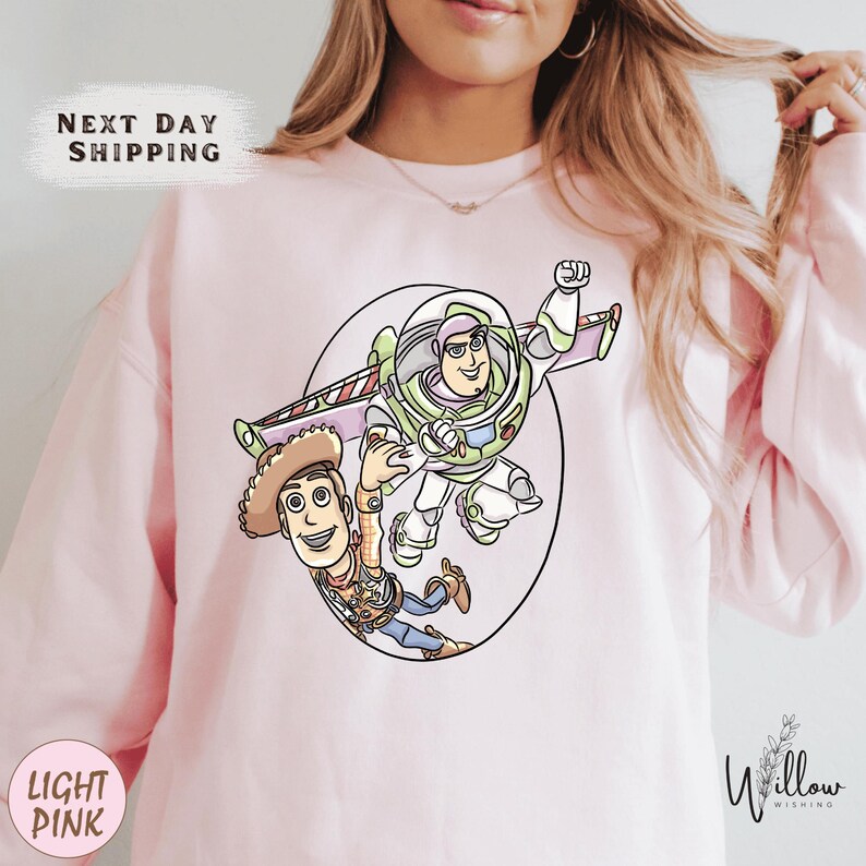 A woman wearing a pink sweatshirt with a cartoon illustration of Buzz Lightyear and Woody from Toy Story.