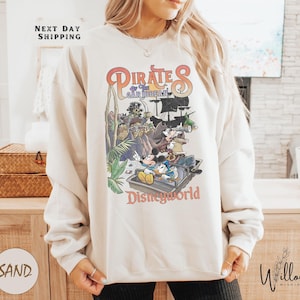 A woman wearing a white sweatshirt with a colorful graphic of Disney characters from the Pirates of the Caribbean franchise.