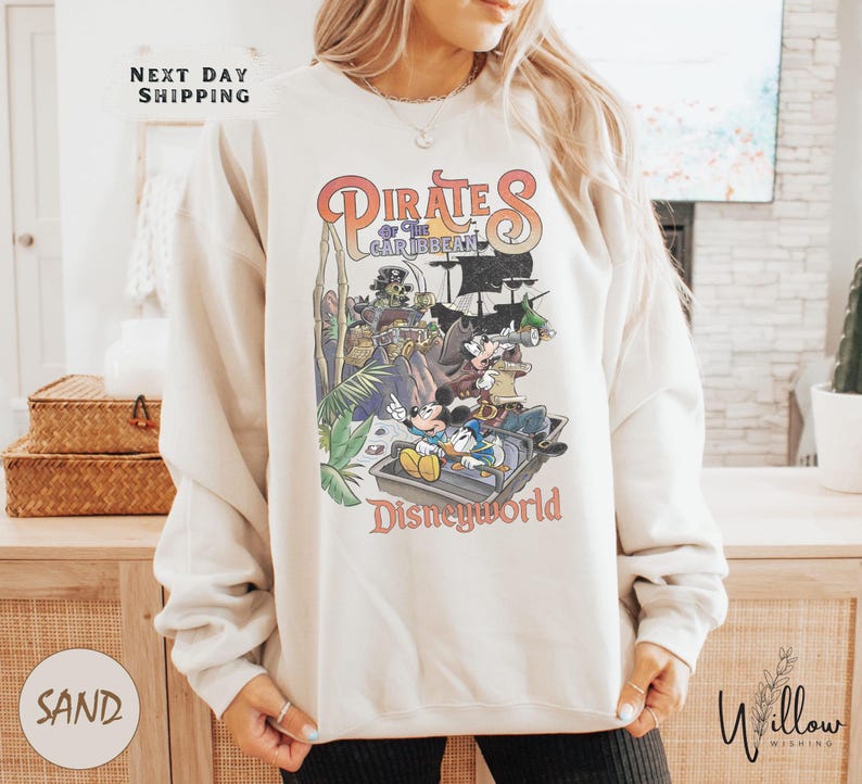 A woman wearing a white sweatshirt with a colorful graphic of Disney characters from the Pirates of the Caribbean franchise.