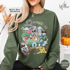 A woman wearing a green sweatshirt with a colorful graphic of Disney characters and a castle on it.