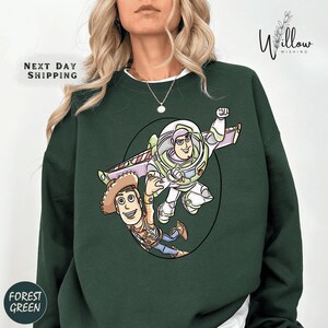 A woman wearing a green sweatshirt with a cartoon illustration of Buzz Lightyear and Woody from Toy Story.