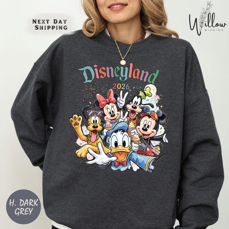 A woman wearing a gray sweatshirt with a colorful graphic of Disney characters from Disneyland.