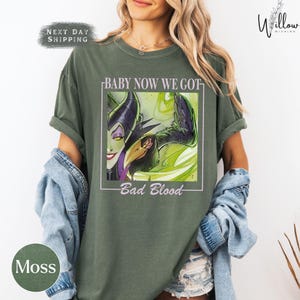 A woman wearing a green t-shirt with a graphic design featuring a character from the "Bad Blood" movie franchise.