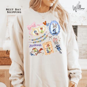 A woman wearing a white sweatshirt with a colorful graphic design featuring cartoon characters and text.