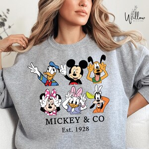 A woman wearing a gray sweatshirt with a graphic of Disney characters Mickey Mouse and Co.