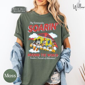 A woman wearing a green t-shirt with a cartoon image of Mickey Mouse and Goofy on a parachute, along with the text "Sky Commander SOARIN' AROUND THE WORLD Fearless Pursuit of Adventure!"