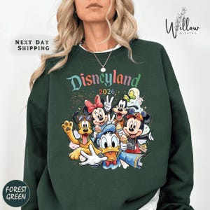 A woman wearing a green sweatshirt with a colorful graphic of Disney characters from Disneyland.
