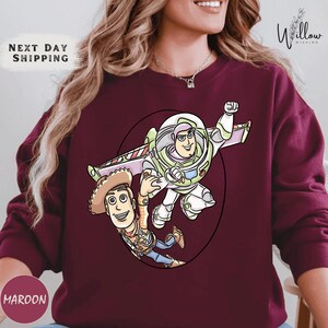 A woman wearing a burgundy sweater with a graphic of Buzz Lightyear and Woody from Toy Story printed on it.