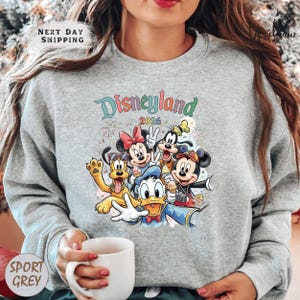 A woman wearing a gray sweatshirt with a colorful graphic of Disney characters from the theme park.