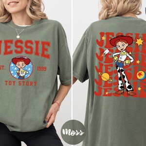 A woman wearing a green t-shirt with a graphic of a character from the Toy Story franchise, specifically named Jessie.