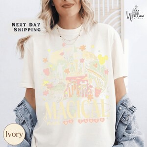 A woman wearing a white t-shirt with a colorful graphic design featuring Disney-themed elements, such as Mickey Mouse and the Eiffel Tower.