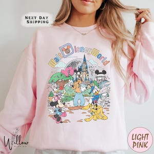 A woman wearing a pink sweatshirt with a colorful illustration of Disney characters and landmarks.