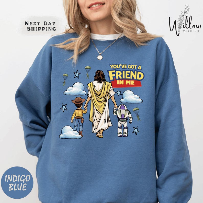 A woman wearing a blue sweatshirt with a cartoon illustration of a woman holding a child and a robot, along with the text "You've got a FRIEND in ME" and a Bible verse reference.