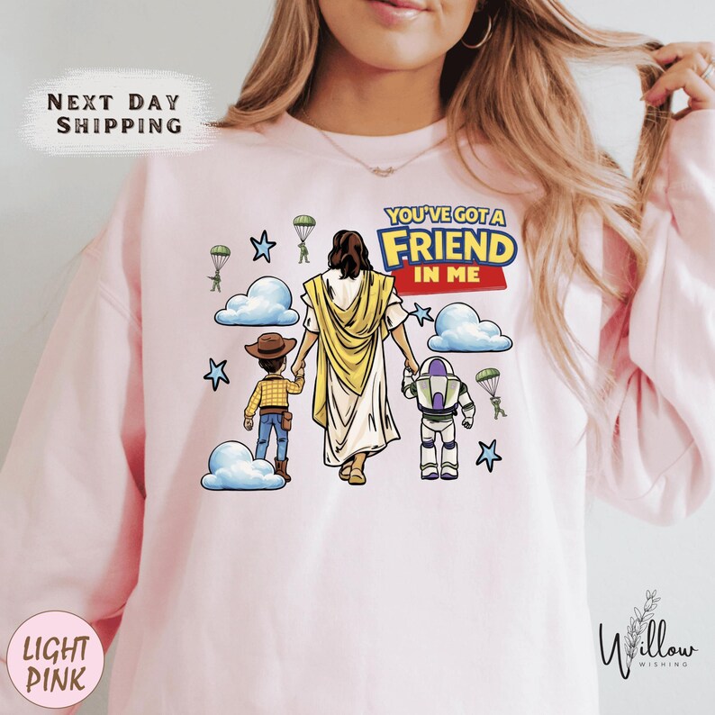 A woman wearing a pink sweatshirt with a cartoon illustration of a person holding hands with a child and a character from Toy Story.