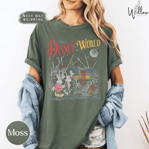 A woman wearing a green t-shirt with a Disney World graphic and text, along with a denim jacket, standing against a white background.
