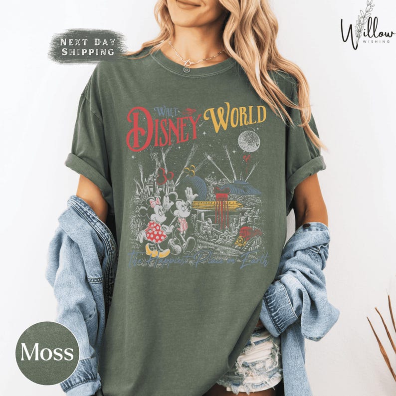 A woman wearing a green t-shirt with a Disney World graphic and text, along with a denim jacket, standing against a white background.