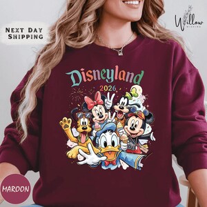 A woman wearing a maroon sweater with a colorful graphic of Disney characters from Disneyland.