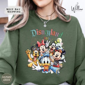 A green sweatshirt with a colorful graphic of Disney characters from the theme park, including Mickey Mouse, Donald Duck, Goofy, Minnie Mouse, and Pluto.