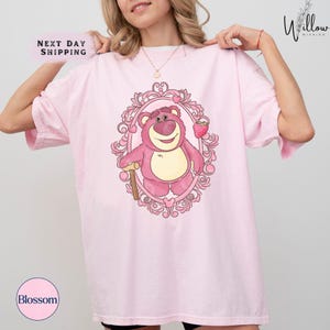 a woman wearing a pink t - shirt with a pink teddy bear on it