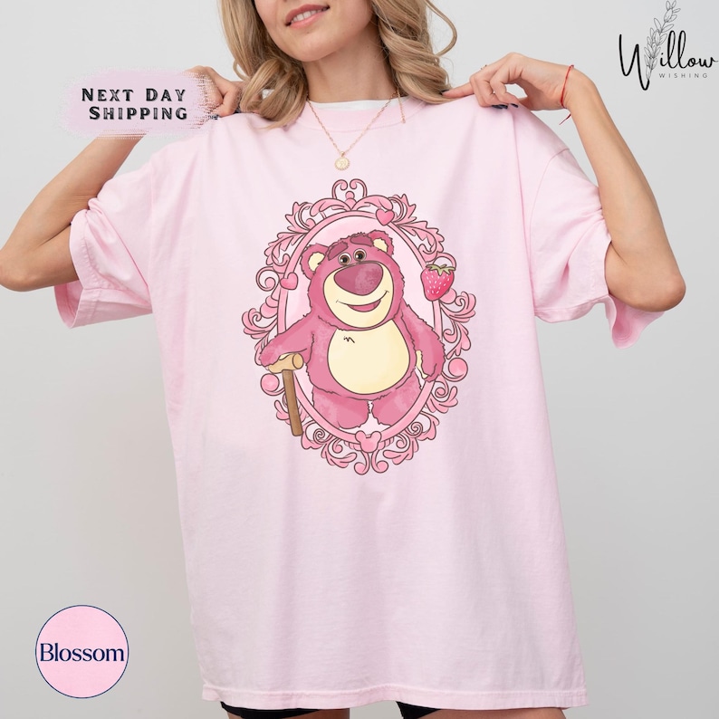 a woman wearing a pink t - shirt with a pink teddy bear on it