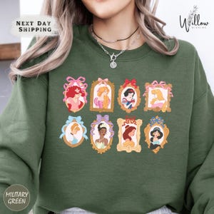 A woman wearing a green sweatshirt with a collage of illustrations of Disney princesses.
