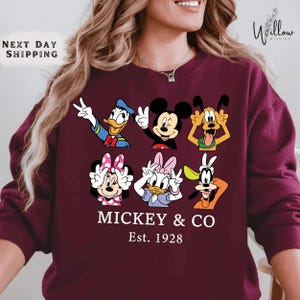 A woman wearing a maroon sweater with a graphic design featuring the Disney characters Mickey Mouse and Donald Duck.