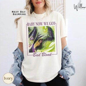 A woman wearing a white t-shirt with a graphic design featuring a character from the Disney movie "Bad Blood".