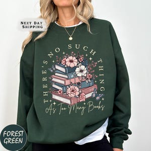 May include: Forest green sweatshirt with the text "There's No Such Thing As Too Many Books" surrounding a stack of books and flowers. The books are in shades of pink and blue, with pink and white flowers and butterflies.