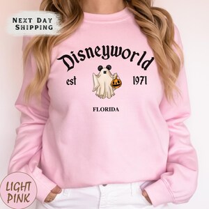 a woman wearing a pink disney world sweatshirt