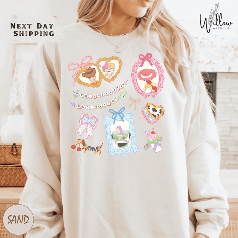 A woman wearing a white sweatshirt with a colorful graphic design featuring various cartoon-style illustrations, including hearts, bows, and other whimsical elements.