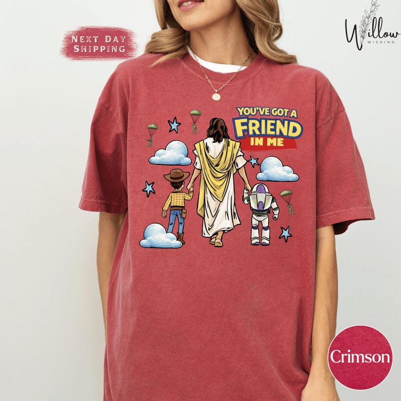 A woman wearing a red t-shirt with a graphic design depicting a cartoon illustration of a woman and a child, along with various other elements such as clouds, stars, and a Bible.