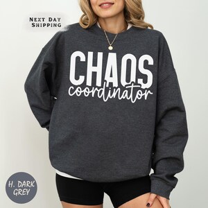 a woman wearing a black sweatshirt with the words chaos on it