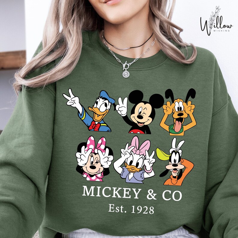 A woman wearing a green sweatshirt with a graphic of Disney characters Mickey Mouse and Donald Duck.