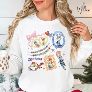 A woman wearing a white sweatshirt with a colorful graphic design featuring various cartoon characters from the movie "Zootopia".