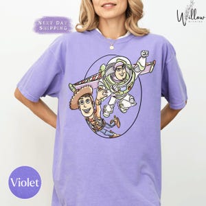 A woman wearing a purple t-shirt with a cartoon image of Buzz Lightyear and Woody from Toy Story printed on it.