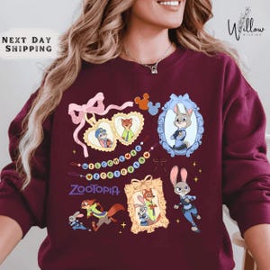A woman wearing a burgundy sweatshirt with various cartoon animal characters and a mirror frame.